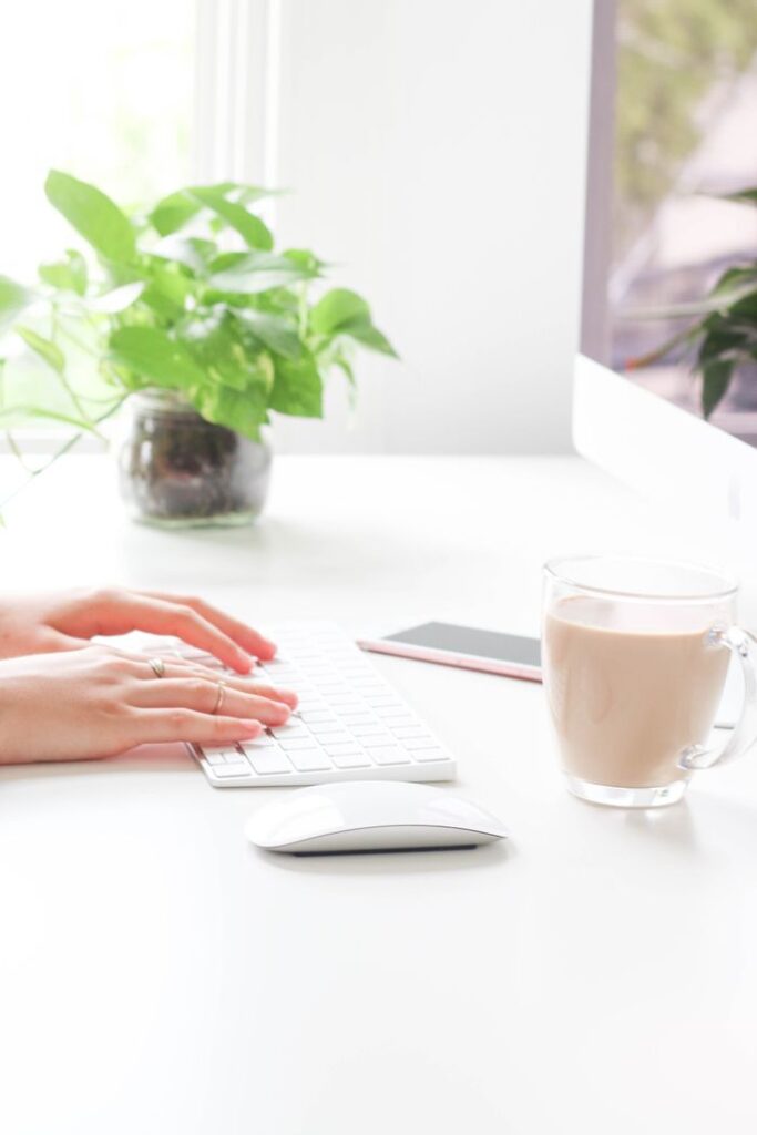 A woman working from home, typing on a keyboard with coffee nearby.