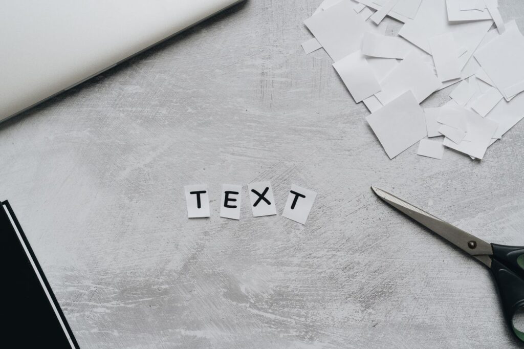 A flat lay of a creative workspace featuring cutout text, scissors, and paper pieces on a textured surface.